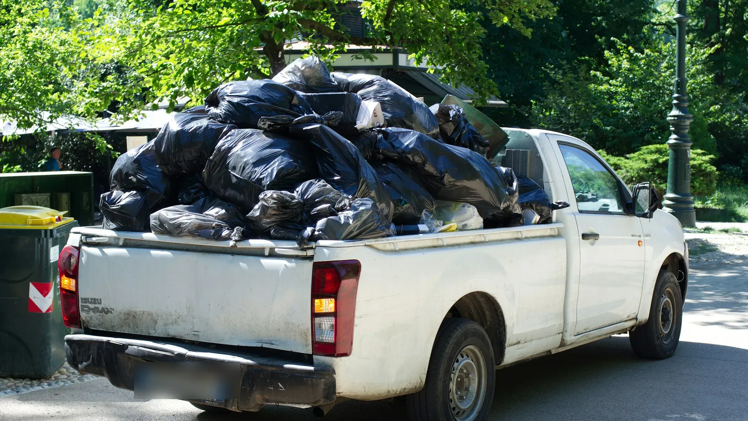 A white pickup truck at a kerb, its open bed piled high with tied black rubbish bags.